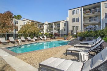 A swimming pool with lounge chairs in front of an apartment building